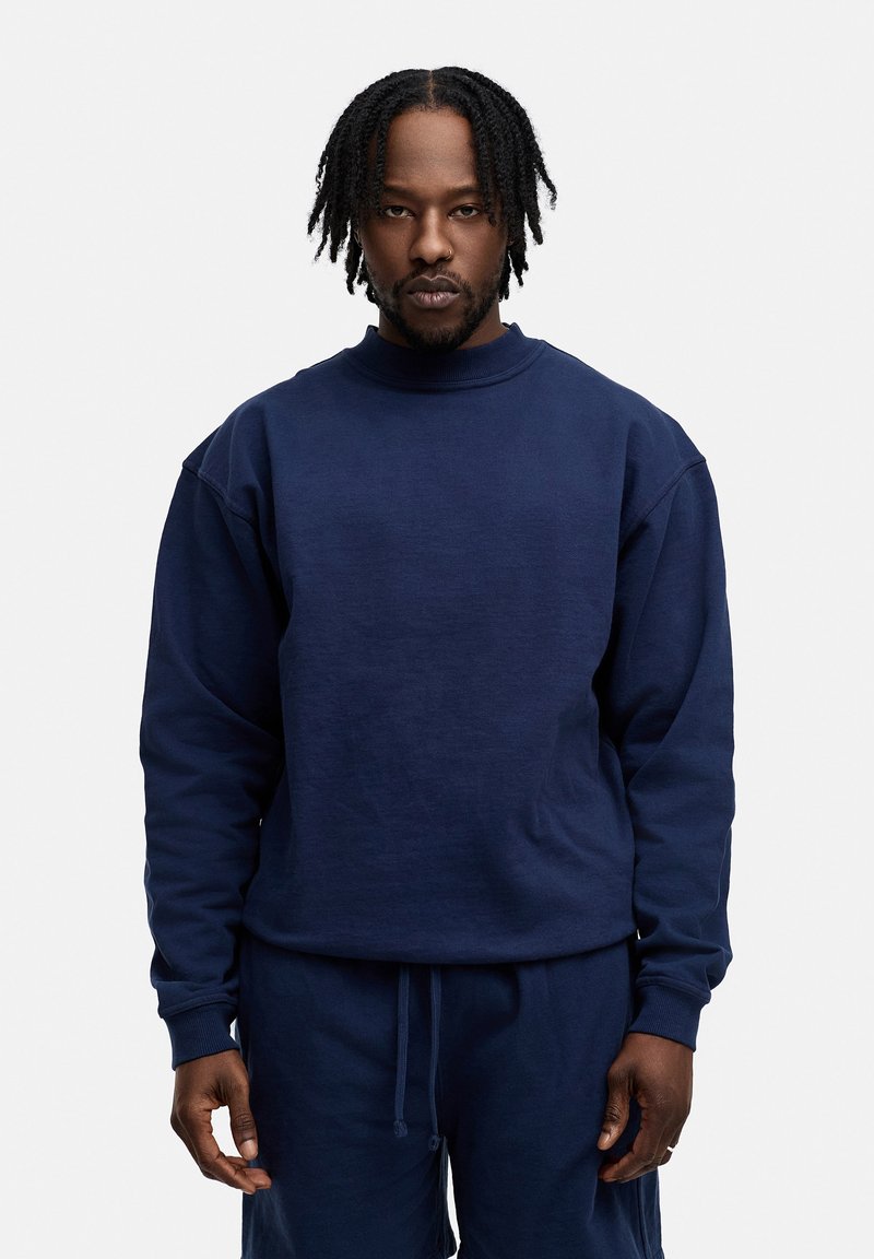 Marineblauer Baumwollpullover mit ribbeligem Rundhalsausschnitt und langen Ärmeln, der einen lässigen Schnitt und eine strukturierte Textur aufweist.