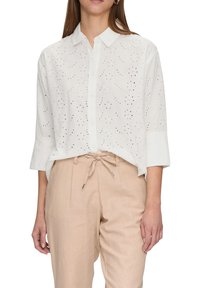 White button-up shirt with floral eyelet pattern, collared neckline, and three-quarter sleeves, paired with light beige drawstring trousers.