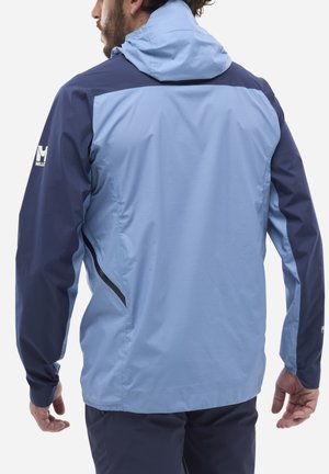 Man wearing a two-tone light and dark blue hooded jacket, shown from the back with arms relaxed at sides.