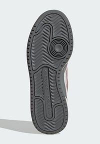 Black rubber sneaker sole with zigzag traction pattern, textured surface, and a visible logo. Features a circular design element near the center.