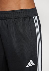 Czarne sportowe szorty z teksturowanej tkaniny, elastycznym pasem i trzema białymi pionowymi paskami po boku oraz logo w rogu.