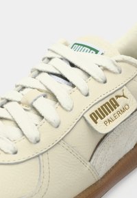 PUMA Palermo tenisice imaju kremastu kožnu gornjište, bijele vezice, zlatni logo dodatak i teksturiranu smeđu gumenu potplat.
