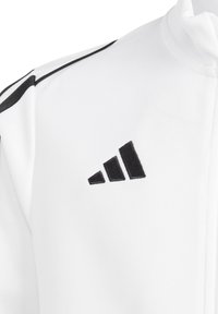 White sports jacket with black stripes and a signature black three-stripe logo embroidered on the left chest area. Smooth texture.