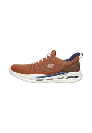 Zapatilla de malla marrón con cordones y suela blanca. Presenta un cuello de color azul marino, un logo lateral y detalles de "Arch Fit" en la suela.