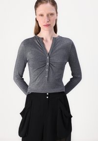 Gray long-sleeve top with buttoned placket and gathered front detail, paired with black shorts featuring large side pockets and button accents.