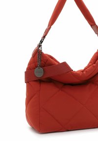 Red quilted fabric handbag with a soft, rounded shape. Features a wide strap and a metallic tag with chain detail. Smooth texture.