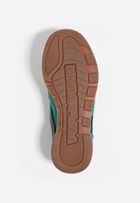 Suela de zapato con una base de goma texturizada en marrón, con la marca "BIMBA Y LOLA" grabada. Acentos coloridos en verde azulado y negro presentes en los lados.