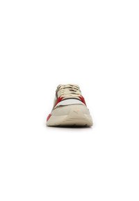 Chaussure de sport beige clair avec des accents rouges et gris. Tige texturée en tissu et daim. Semelle blanche épaisse avec rainures. Système de laçage classique.