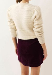 Cremefarbener Strickpullover mit strukturiertem Muster und Puffärmeln, kombiniert mit einem dunkelvioletten Cordrock. Enganliegendes Design, gerippte Bündchen.
