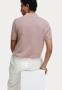Kortærmet polo skjorte i bl�ød pink med krave og hvidt kant, parret med hvide bukser. Glat tekstur og afslappet pasform.