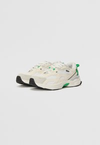 Sneaker bianche con accenti verdi, realizzate in materiale reticolato e suede, con suola spessa, design con lacci e dettagli testurizzati sui lati.