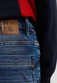 Jeans av denim med en blå denimtextur, med kontrastsömmar, en läderetikett märkt 'BLUE RIDGE' och en detalj på bakfickan.