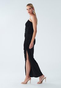Schwarzes trägerloses Kleid mit Raffung, einem seitlichen Schlitz und einer fließenden Silhouette, aus glattem Stoff gefertigt, kombiniert mit klaren High Heels.