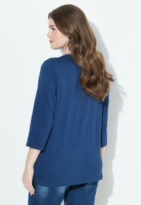 Tmavě modrý dlouhý rukáv top s volným střihem a kulatým výstřihem. Měkká, lehká látka s texturovaným vzhledem.