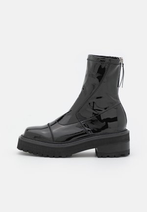 Bottine à cheville en cuir patenté noir brillant avec semelle épaisse, talon bloc, panneaux cousus et fermeture éclair à l'arrière avec languette de tirage.
