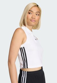 Biała bezrękawnikowa bluzka polo z kołnierzykiem, z czarnymi trójpaskowymi akcentami po bokach. Tkanina wygląda na gładką i dopasowaną.