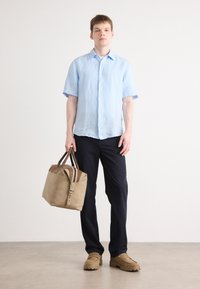 Light blue short-sleeve linen shirt, navy pants, beige bag with brown accents, and tan shoes with rubber soles, against a light background.