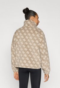 Ζακέτα από φλις με ψηλό γιακά και μπεζ φόντο με ελαφρύ μοτίβο λογοτύπου. Μαλακή υφή και ελαφρώς φαρδιά σχεδίαση.