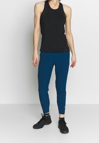Svart ärmlös topp med böjda sömmar, parat med blå tajta leggings. Texturerad tyg. Svarta träningsskor fulländar outfiten.