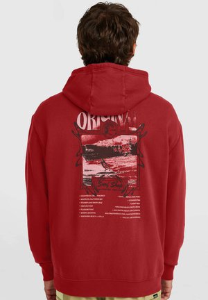 Sudadera con capucha roja con un estampado gráfico que muestra una escena de surf y texto. El material parece suave, con un ajuste estándar y capucha con cordón.