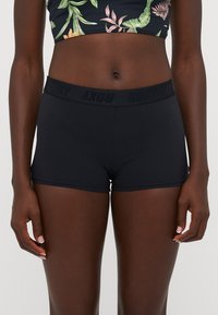 Schwarze Sportshorts mit einem elastischen Bund, auf dem das Wort "ROXY" in dunkler Schrift steht. Der Stoff ist glatt und enganliegend.