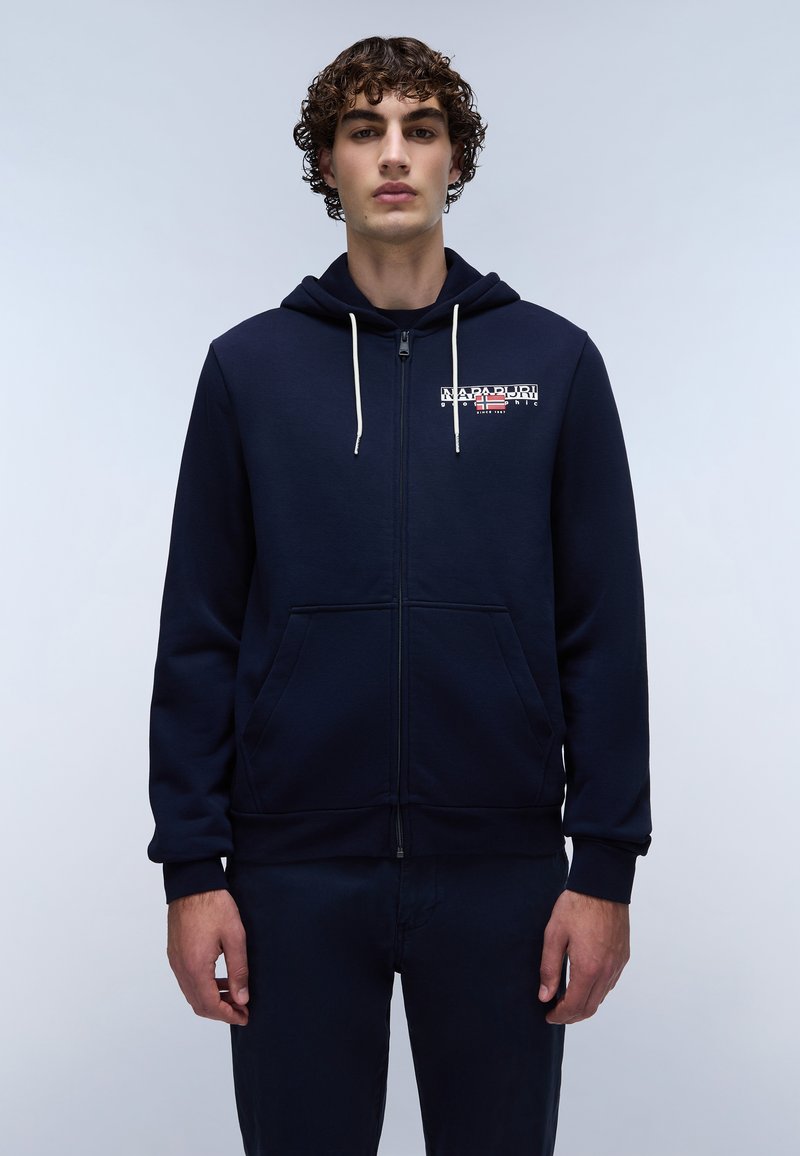 Felpa zip con cappuccio in navy, dotata di cordoncino, tasche frontali e dettaglio logo sul petto; il tessuto ha una texture liscia e una vestibilità confortevole.