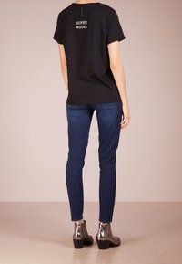 Camiseta de algodón negra con el texto "SUPER MODEL" en blanco en la espalda, combinada con unos vaqueros azul oscuro y botas metálicas hasta el tobillo.