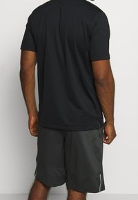 Musta lyhythihainen urheilupaita kevyestä materiaalista, yhdistettynä tummanharmaisiin urheilushortseihin, joissa on valkoisia yksityiskohtia.