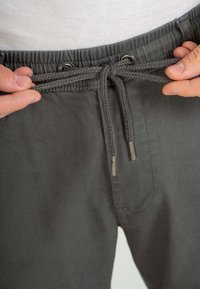 Pantalones grises con cintura elástica, con cordón trenzado y ojales de metal. Textura suave con un detalle de costura simple.