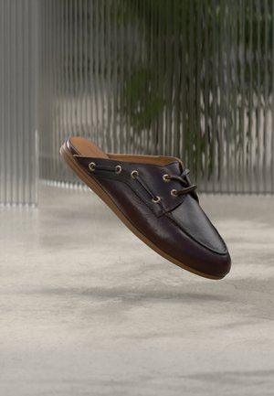 Pantof maro închis din piele, slip-on, cu șireturi și orificii metalice, plutind deasupra unui podea din beton gri, cu un fundal translucid texturat.