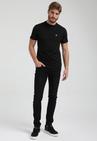 Melns kreklu ar apaļu kakla izgriezumu, izgatavots no kokvilnas, valkāts kopā ar melnum slim-fit džinsiem un melniem sporta apaviem. Iezīmēts ar mazu logo uz krūtīm.