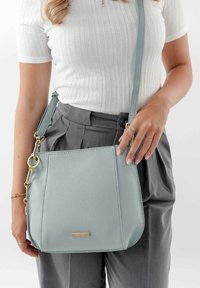 Borsa a tracolla in pelle azzurro chiaro con una finitura testurizzata, dotata di dettagli in metallo dorato e una lunga tracolla regolabile.