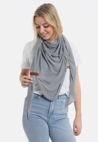 Grijze, gestructureerde sjaal om iemands nek; voorzien van houten en metalen hardware accenten; gecombineerd met een wit shirt en blauwe jeans.