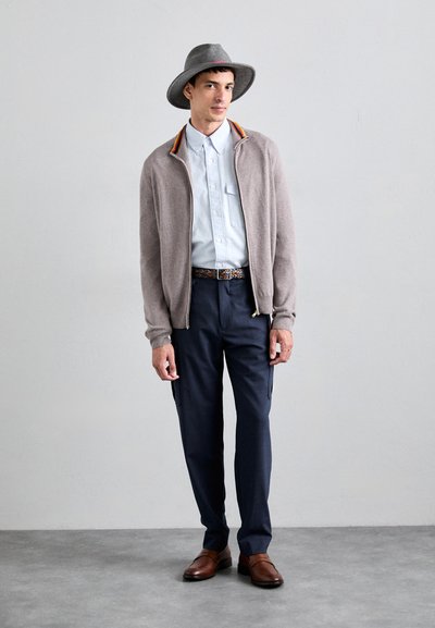 Light gray wool cardigan with colorful accents, light blue button-up shirt, dark navy cargo pants, brown leather shoes, and gray wide-brim hat.