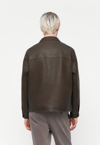 Chaqueta de cuero marrón con un collar clásico y silueta recta. Presenta una textura suave y detalles de costura sutiles en la parte posterior.
