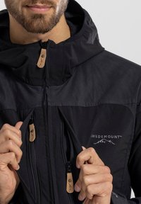 Giacca nera con tasche con zip, linguette in pelle e colletto alto. Presenta un logo sul petto e un design del tessuto testurizzato.