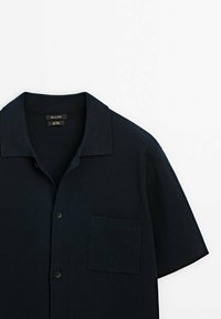 Koszula z krótkim rękawem, w kolorze navy blue, zapinana na guziki, wykonana z teksturowanej tkaniny, z płaskim kołnierzykiem i kieszonką na lewej piersi. Posiada czarne guziki.
