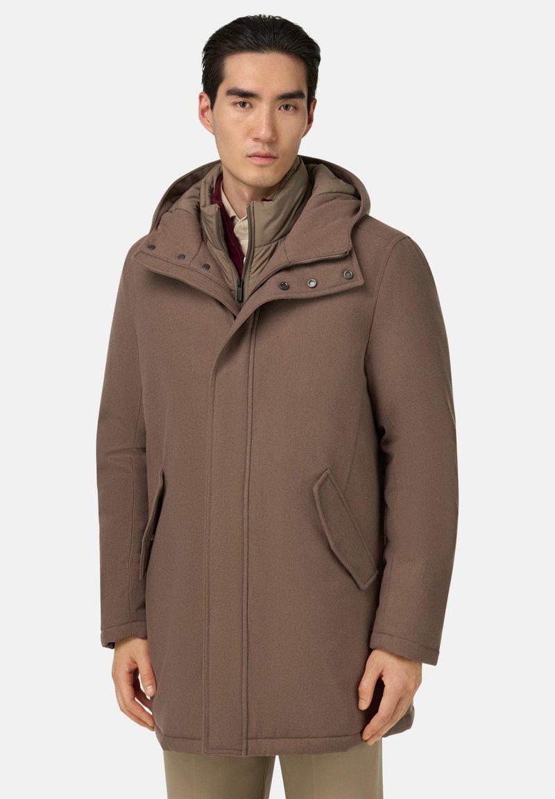 Manteau à capuche marron avec fermeture éclair, poches latérales et texture lisse. La couche intérieure est de couleur beige clair avec une fermeture éclair et un col montant.