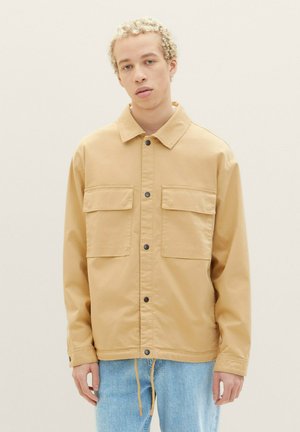 Tan, long-sleeve jacket featuring two chest pockets, button closures, and a drawstring at the hem. Made of smooth fabric with a casual fit.