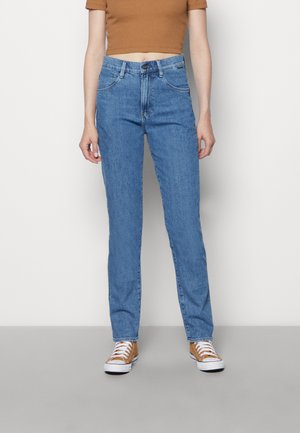 Μπλε τζιν παντελόνι με ίσια κοπή, διαθέτει μπροστινές τσέπες και κουμπί κλεισίματος. Φοριέται με καφέ cropped top και αθλητικά παπούτσια.