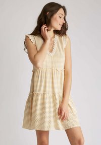 Robe courte à carreaux jaunes et blancs avec un col volanté, des manches courtes et une jupe à volants, fabriquée en tissu léger et texturé.