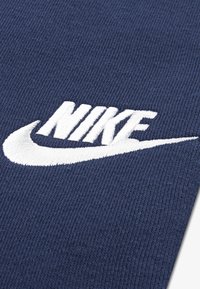 Material albastru marin cu un logo Nike alb brodat proeminent, cu un design curbat în formă de swoosh și suprafață texturată.