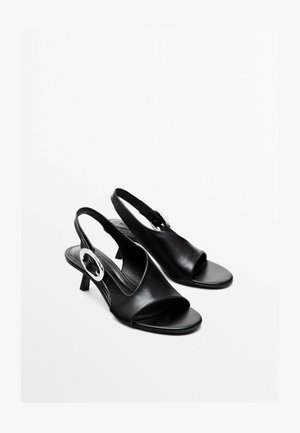 Black leather slingback sandals with an open toe, low heel, and silver circular hardware accent on the side. Smooth texture and simple design.