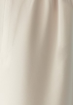 Tela beige con una textura fina y un brillo sutil, mostrando pliegues naturales y un detalle de costura vertical en el lado izquierdo.