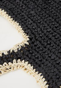Gros plan sur un tissu noir tissé avec une bordure tissée de couleur naturelle, montrant des fibres épaisses, texturées et entrelacées ainsi que des coutures détaillées.
