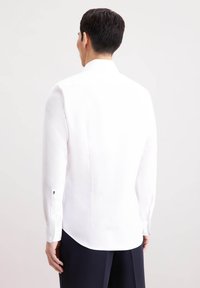 Camicia bianca a maniche lunghe con vestibilità sartoriale, dotata di colletto, spacchetti laterali all'orlo e ricami neri sui polsini.