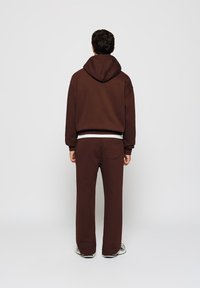 Brauner Hoodie mit großer Kapuze, kombiniert mit braunen Jogginghosen. Der Stoff ist weich und die Hose verfügt über eine Gesäßtasche.