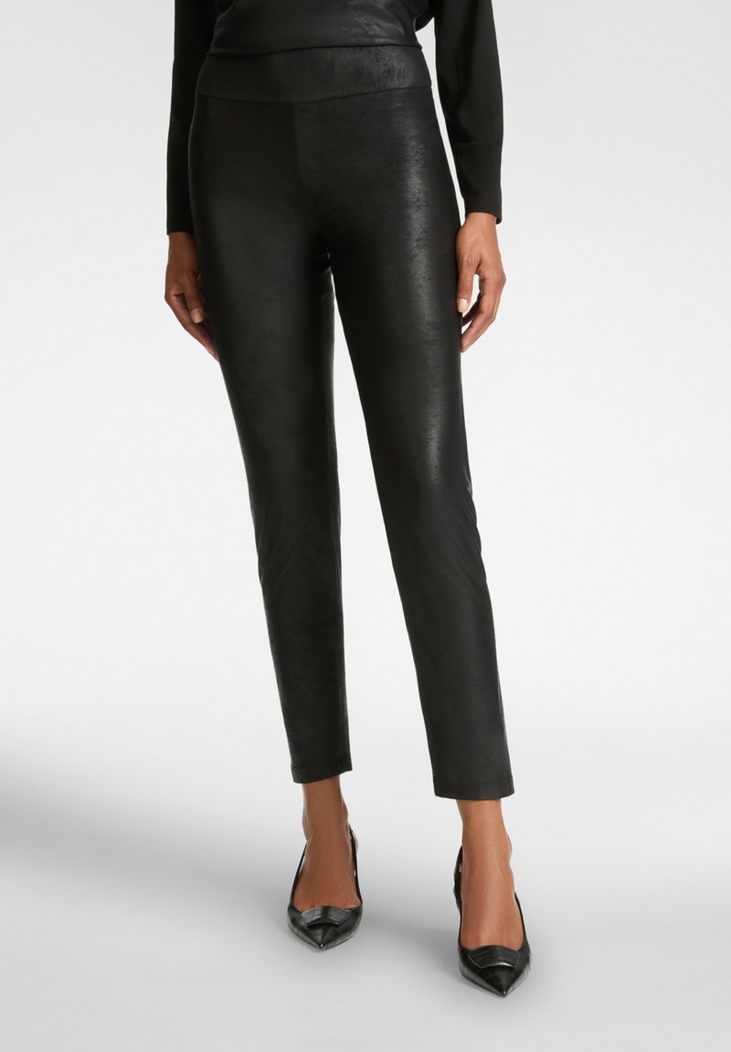 Zwarte faux leren broek met een slanke, glanzende textuur, een aansluitend ontwerp en een hoge tailleband. Gepaarde met puntige zwarte hakken.