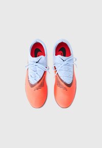 Sportschoenen met een gestructureerde oranje bovenkant, een lichtblauwe kraag, een zwart Nike-logo en witte veters. De zool is plat en flexibel.
