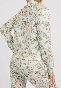 Bloementrainingspak in lichtgroene stof met roze en blauwe bloemenpatronen, lange mouwen en een elastische tailleband voor comfort.